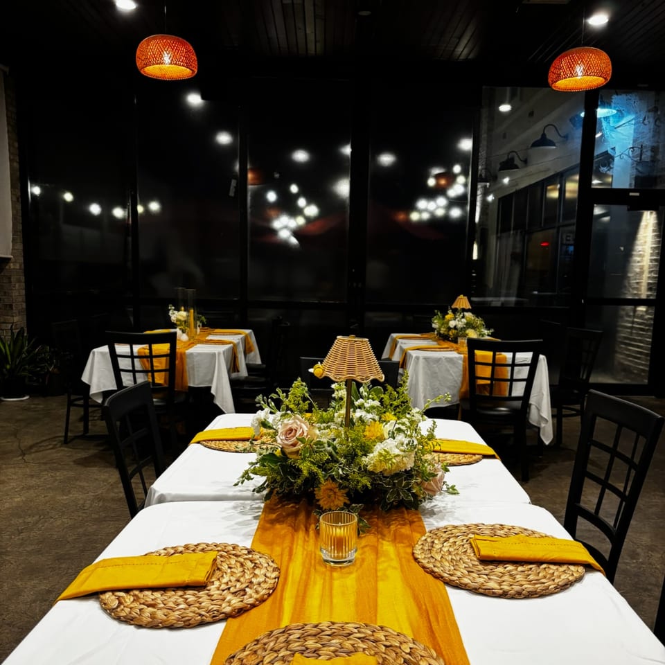 Restaurant dining room with tables set with white tablecloths, yellow runners, and floral centerpieces.
