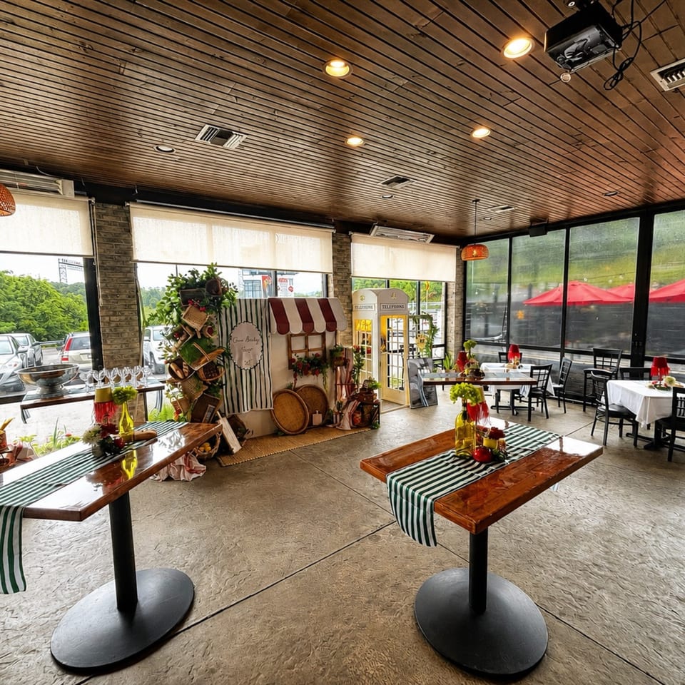 Restaurant interior with wooden ceiling, decorated tables, and a charming market stall display by large windows.