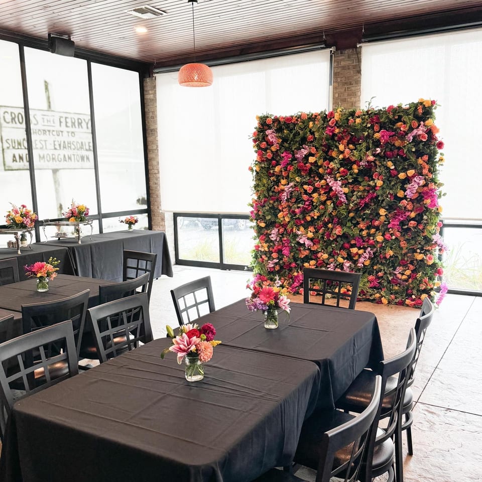 Kavel's Restaurant & Venue dining room with black tables, chairs, and a vibrant floral wall.