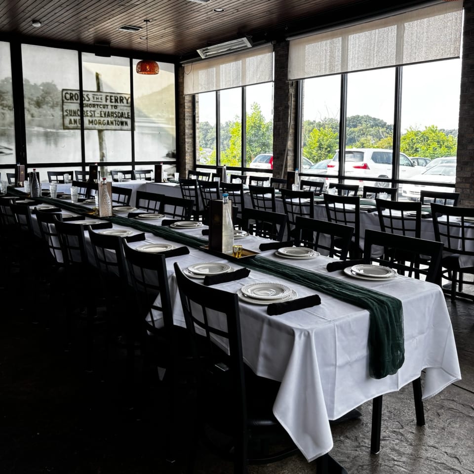 Long dining tables set with white tablecloths, dark green runners, and black chairs in a restaurant.
