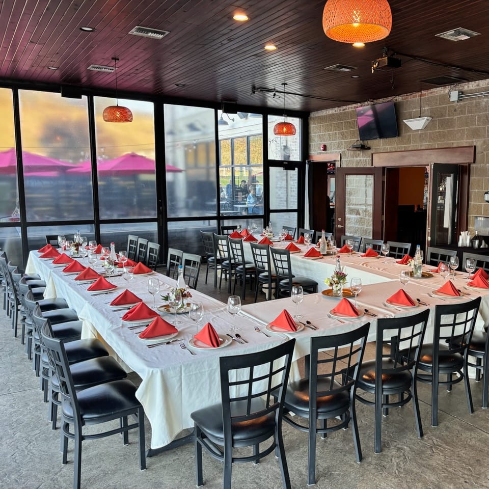 U-shaped dining table set with red napkins and wine glasses, overlooking an outdoor patio.