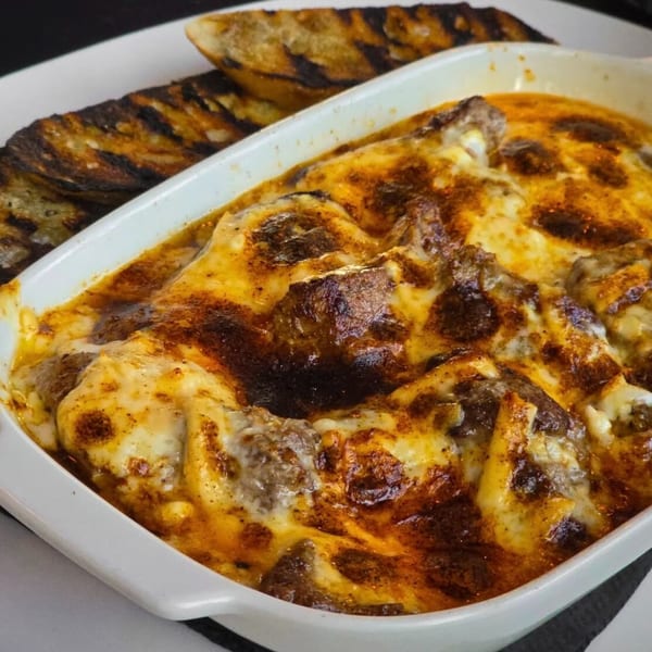Baked meatballs with melted cheese in a white dish, served with grilled bread on the side.