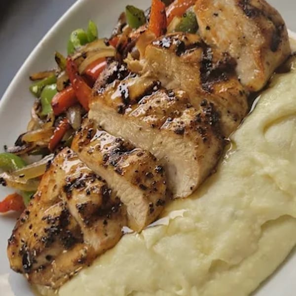 Grilled chicken breast with mashed potatoes and sautéed vegetables on a white plate.