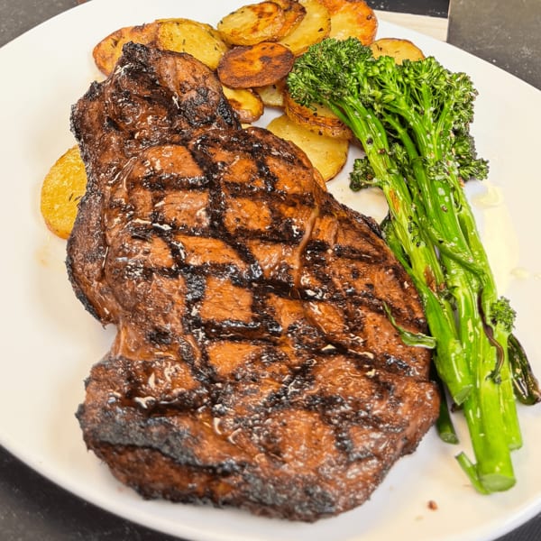 Grilled steak with grill marks, roasted potatoes, and broccolini on a white plate.