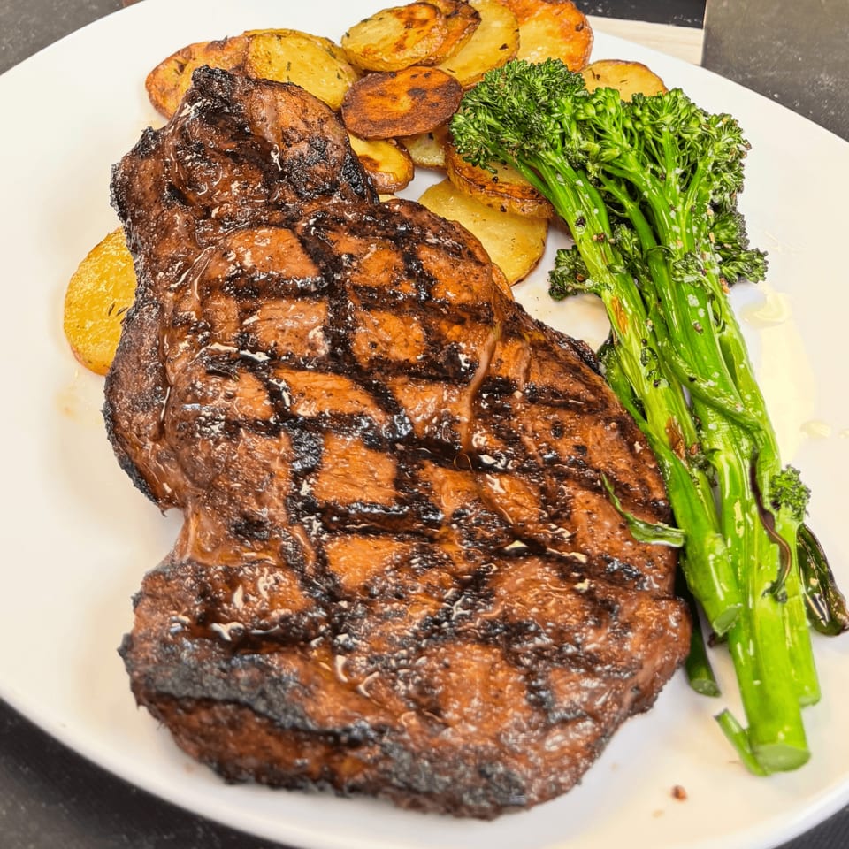 Grilled steak with grill marks, roasted potatoes, and broccolini on a white plate.