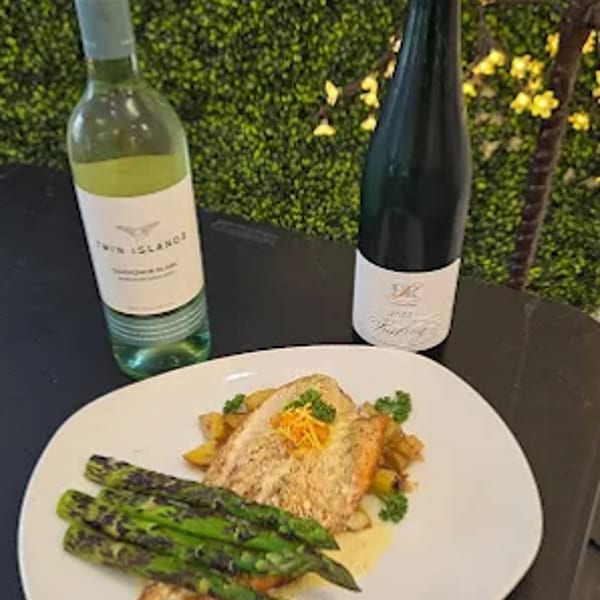Grilled salmon with asparagus and two bottles of wine on a table with a green wall.